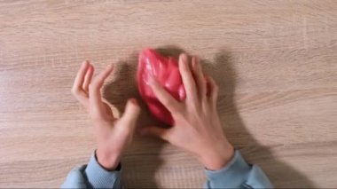 Çamurla oynamak, eğlence ve stres atmak için yapışkan maddeyi germek. Yaklaş ve üst görüntüde kırmızı, parlak balçık tutan ve sıkan kadın elini gör. 4K çözünürlük videosu