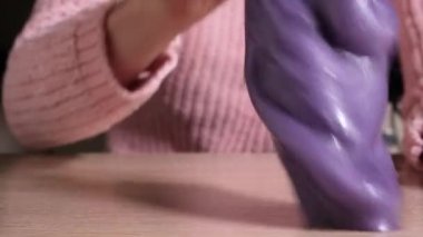 Çamurla oynamak, eğlence ve stres atmak için yapışkan maddeler kullanmak. Yakın çekim ve üst görünümde mavi, pembe ve mor balçık tutan ve sıkan kadın eli görülüyor. Tam HD yavaş çekim videosu.