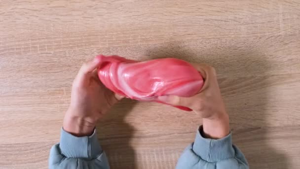 Playing with slime, stretching the gooey substance for fun and stress relief. Close up and top view of female hand holding red and white shining slime and squeezing it. 4K video. — Stock Video