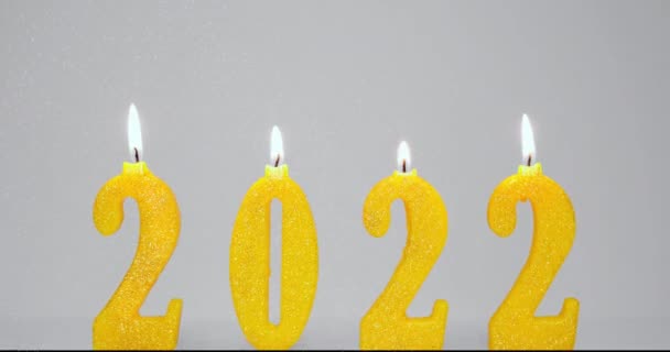 Fondo de vacaciones de velas amarillas encendidas 2022 y partículas de fuegos artificiales. Feliz año nuevo 2022 concepto. Vídeo Full HD en cámara lenta. Quema 2022 velas aisladas sobre fondo gris. — Vídeo de stock