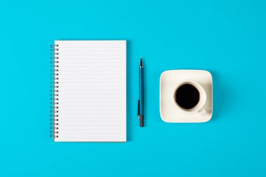 Not defteri, kalem ve açık mavi arka planda izole edilmiş bir fincan kahve. Kopyalama alanı olan not defteri. Ofis, iş, ihtiyatlı stil