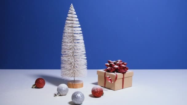 Mooie kerst of Nieuwjaar video banner met kopieerruimte. Speelgoed Kerstboom, geschenkdoos met rode strik en kerstballen op blauwe achtergrond met sneeuw op de achtergrond — Stockvideo