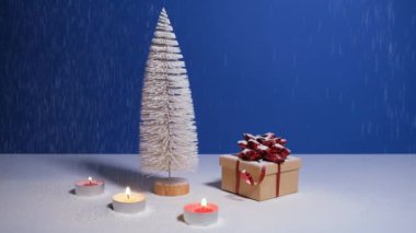Fotokopi alanı olan güzel bir Noel ya da yeni yıl afişi. Oyuncak Noel ağacı, kırmızı fiyonklu hediye kutusu ve mavi arka planda yanan mumlar. Arka planda kar yağıyor..