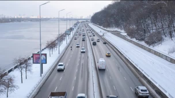 Вид с моста на оживленную городскую дорогу в Киеве и реку Днепр, покрытую льдом, Украина. Городское шоссе в снегу и Днепре. — стоковое видео