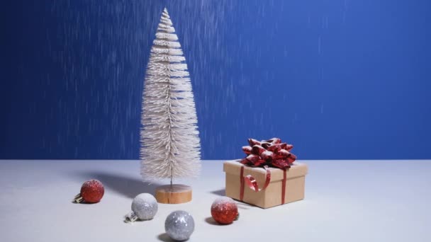 Piękne Boże Narodzenie lub Nowy Rok baner wideo z miejsca do kopiowania. Zabawka choinka, pudełko z czerwonym łukiem i bombki świąteczne na niebieskim tle z śniegiem spada na tle — Wideo stockowe