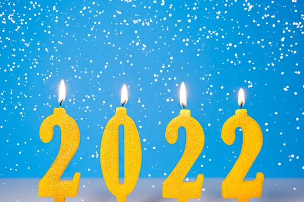 Holiday background of burning yellow canes 2022 Καλή Χρονιά έννοια Καίγοντας κίτρινα και χρυσά 2022 κεριά απομονωμένα σε μπλε φόντο με χιόνι που πέφτει — Φωτογραφία Αρχείου