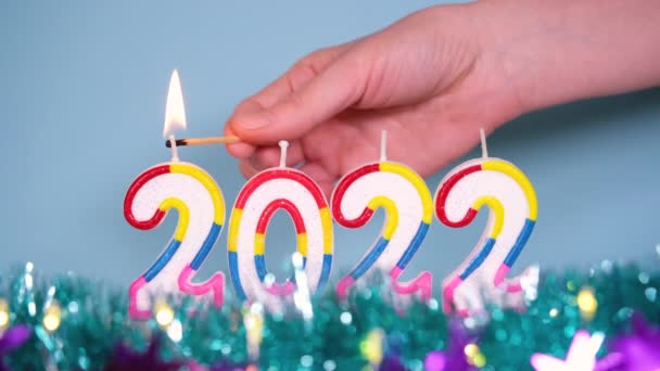 Fond de vacances de l'éclairage à la main bougies colorées 2022 Avec tinsel bleu et lilas. Bonne année 2022 concept. Vidéo en résolution 4K. Brûler 2022 bougies isolées sur fond bleu. — Video