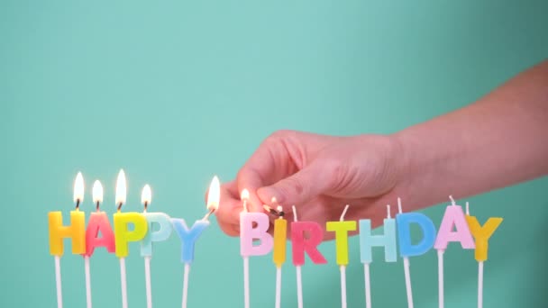 Happy Birthday concept Made of Burning Colorful Candles on blue or turquoise background. Hand lights candles words Happy birthday. 4K resolution video — Stock Video