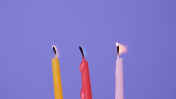 Drie kaarsen uitblazen die branden op een paarse achtergrond. Sluit op blazen uit gele, roze en magenta taart kaarsen. Full HD resolutie slow motion gelukkige verjaardag video. — Stockvideo