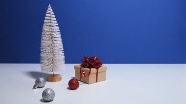 Fotokopi alanı olan güzel bir Noel ya da yeni yıl afişi. Oyuncak Noel ağacı, kırmızı fiyonklu hediye kutusu ve mavi arka planda Noel mücevherleri. Arka planda kar yağıyor.