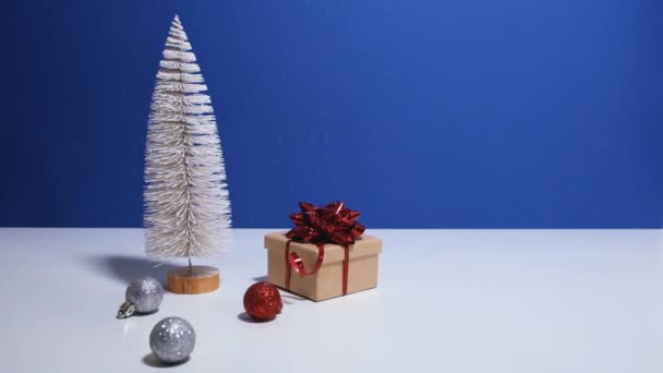 Piękne Boże Narodzenie lub Nowy Rok baner wideo z miejsca do kopiowania. Zabawka choinka, pudełko z czerwonym łukiem i bombki świąteczne na niebieskim tle z śniegiem spada na tle — Wideo stockowe
