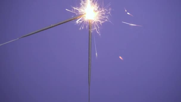 Sparklers acendem a partir de um sparkler. Feche a bandeira de Brilhante queimando três faíscas em um fundo violeta ou roxo. Feliz Natal ou Feliz Ano Novo conceito. Vídeo de resolução 4k — Vídeo de Stock
