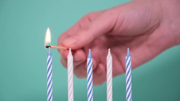 Ruka zapaluje pět svíček izolovaných na modrém nebo tyrkysovém pozadí. Happy Birthday koncept Made of Burning barevné svíčky. Pálení 5 let výročí narozeninové svíčky — Stock video