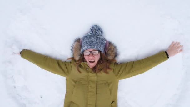 Ung kvinna som gör snö ängel och skrattar. Vinter utomhus aktiviteter. Slow motion full HD-video. — Stockvideo