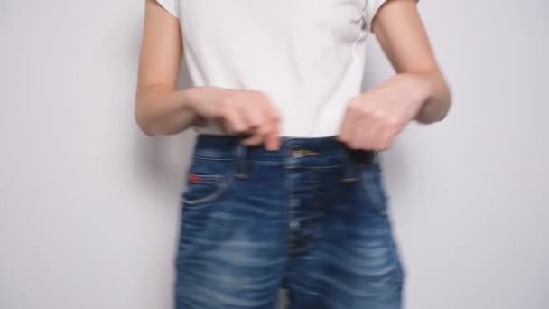 Donna felice che balla in jeans oversize su sfondo bianco. Il concetto di dieta, corretta alimentazione, perdita di peso e il corpo positivo. Slim donna mostrando sciolto jeans e la sua perdita di peso — Video Stock