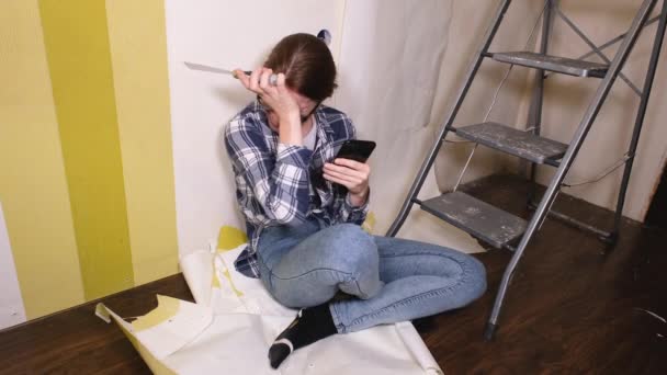 En ung designer flicka sitter i en lägenhet där renoveringar sker och skrattar okontrollerat. 4k upplösning video banner — Stockvideo