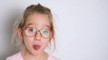 Gözlüklü ve pembe tişörtlü küçük kız eğleniyor ve kameraya yüzünü gösteriyor. Kopyalama alanı olan 4K çözünürlüklü video pankartı