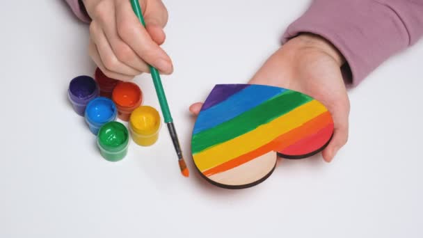 Рука рисует деревянное сердце в цветах гей-прайд-флага. Красочный символ ЛГБТКИИ. Видеобаннер 4K-разрешения — стоковое видео