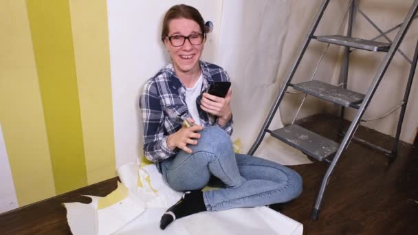 Seorang gadis desainer muda duduk di sebuah apartemen di mana renovasi berlangsung dan tertawa tak terkendali. Banner video resolusi 4k — Stok Video