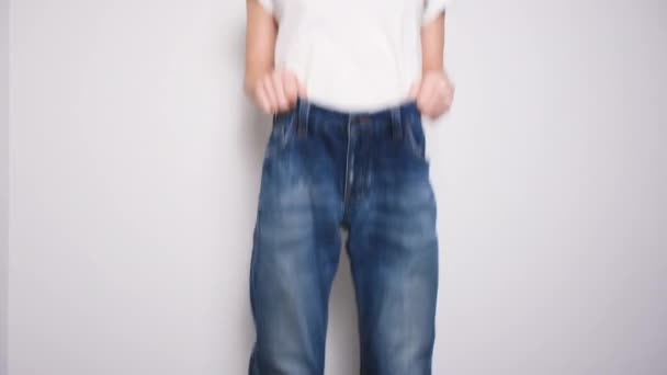 Mujer feliz bailando en jeans de gran tamaño sobre fondo blanco. El concepto de dieta, nutrición adecuada, pérdida de peso y el cuerpo positivo. Mujer delgada mostrando pantalones vaqueros sueltos y su peso de pérdida — Vídeos de Stock