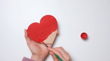 Elleri ahşap bir kalbi kırmızıya boyuyor. 4K çözünürlük video pankartını kapat. Sevgililer Günü için DIY konsepti, Uluslararası Kadınlar Günü veya Anneler Günü