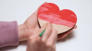 Elleri ahşap bir kalbi kırmızıya boyuyor. 4K çözünürlük video pankartını kapat. Sevgililer Günü için DIY konsepti, Uluslararası Kadınlar Günü veya Anneler Günü