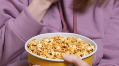 Oturma odasında film izlerken bir kadının elini tutarken ve patlamış mısır yerken yakın plan görüntüsü.