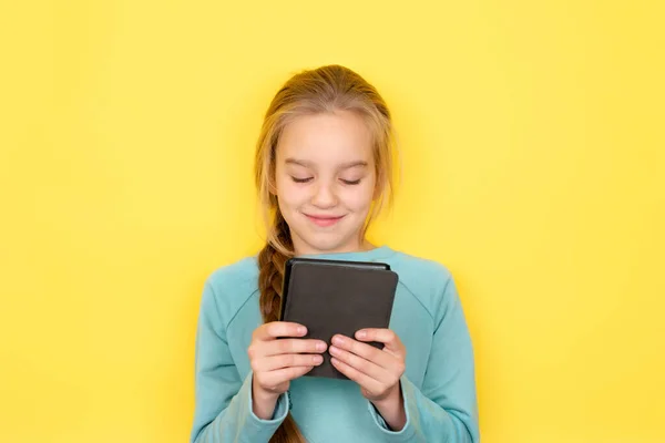 Adolescenta citește cu entuziasm o carte electronică izolată pe fundal galben. Fata folosind dispozitiv tabletă, citind e-book, surfing social media — Fotografie, imagine de stoc