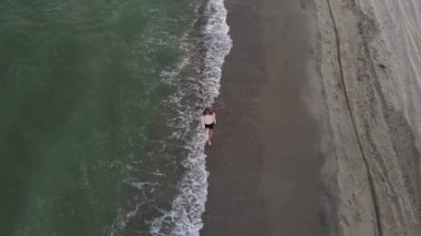 Güzel çıplak ayaklı kadın ıssız sahilde yürüyor. Deniz sahilinde, sahil şeridinde ve yürüyen kızda insansız hava aracı görüntüsü. 4K çözünürlük videosu.