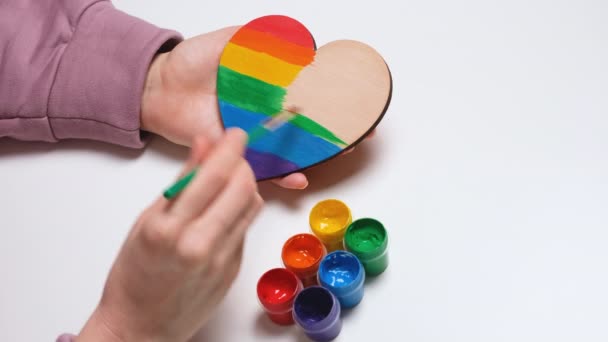 Hand paints a wooden heart in colors of Gay Pride Flag. Colorful symbol of LGBTQIA. 4K resolution video banner — Stock Video
