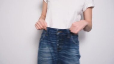 Beyaz arka planda büyük beden kot pantolonla dans eden mutlu kadın. Diyet konsepti, düzgün beslenme, kilo kaybı ve vücut pozitifliği. Sıska Kadın Gevşek Kotları ve Zayıflığını Gösteriyor