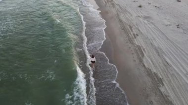 Güzel çıplak ayaklı kadın ıssız sahilde yürüyor. Deniz sahilinde, sahil şeridinde ve yürüyen kızda insansız hava aracı görüntüsü. 4K çözünürlük videosu.