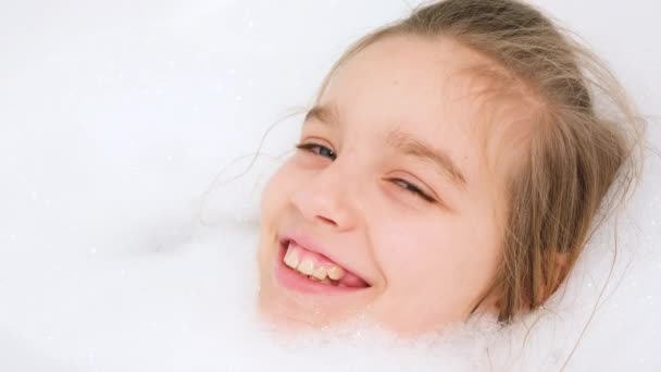Porträtt av glad tonåring flicka som ligger i bad med tjockt tvålskum och tittar i kameran. Begreppet barnhygien och hälsovård i hemmet. Barn som har roligt och leker hemma — Stockvideo