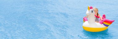 Turkuaz deniz suyunun arka planında beyaz ve pembe renkli tek boynuzlu at üzerinde yüzen kız çocuğu. Sonsuz mavi havuz suyunun arka planında şişme midilli üzerinde yüzen kız..