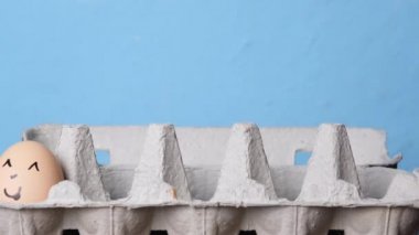 Mavi arka planda yumurta tepsisine gülümseyen yumurtalar katlıyor. Paskalya konsepti. Paskalya 'nın kültürel sembolü. Yüzleri çizilmiş çiftlik yumurtaları.