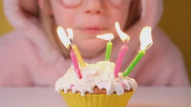 Happy child girl in pink Overalls blowing out five candles on birthday cake at party. Close up on girl face in glasses. Slow motion happy birthday video banner