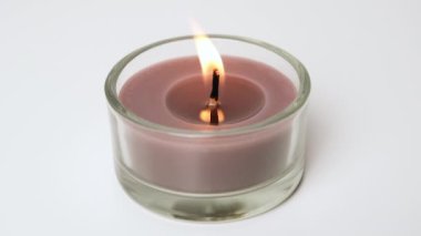 Round brown single Candle flickering on white background. Side view. Candle in glass candle holder burning on the light background. Slow motion full HD video