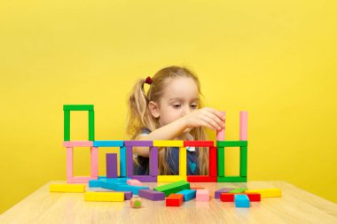 Blond Child Girl playing with wooden blocks. Happy Child playing with wooden construction set. Early development concept.