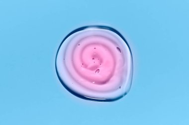 Light blue and pink round gradient transparent gel drop isolated on blue background. Top view. Virus protection or cosmetics concept. Face Serum texture close up.
