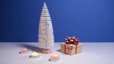 Beautiful Christmas or New Year video banner with copy space. Toy Christmas tree, gift box with red bow and burning candles on blue background.