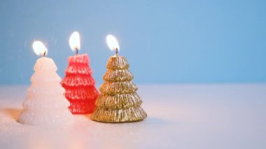 Altın, beyaz ve kırmızı Noel ağacı mumuna kar yağarken mavi arka planda yanan mum ya da fotokopi alanı olan Noel videosu afişi.
