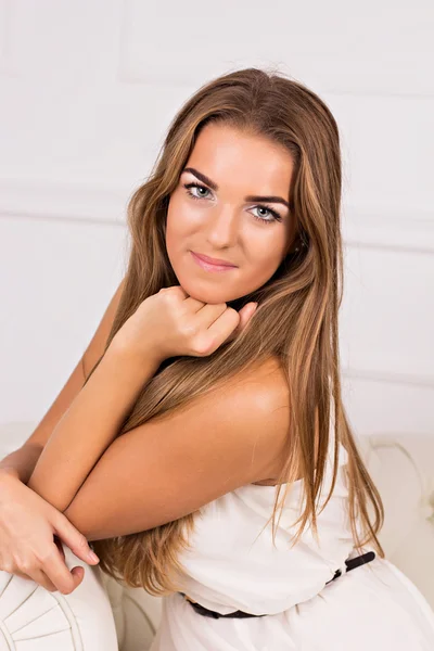 Young blond beautiful girl in white dress sitting on a white cou — Stock Photo, Image