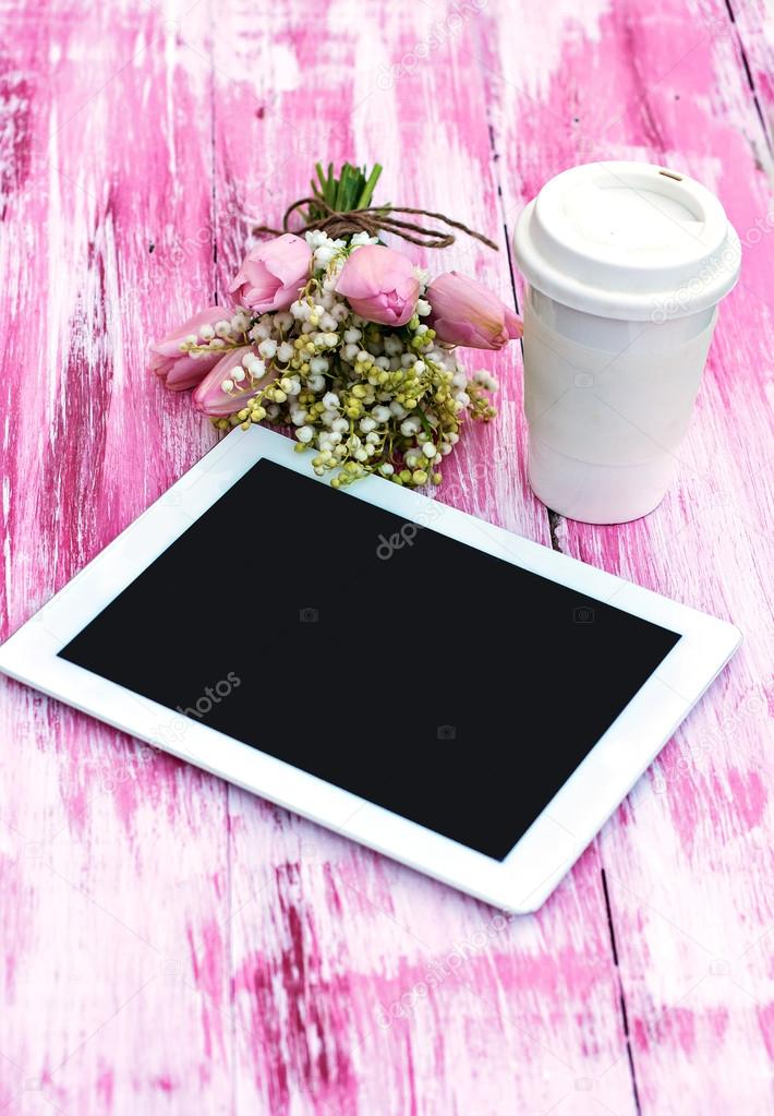 a tablet computer, a glass of coffee and  lilies of valley and t