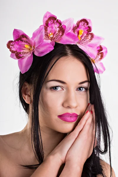 Mooie jonge vrouw in een krans van roze orchideeën — Stockfoto