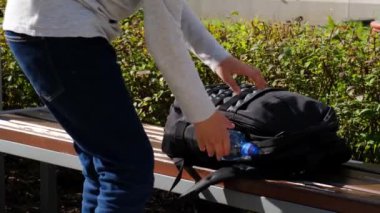 Sarışın çocuk okul çantasından bir şişe su alıp susuzluktan içiyor.