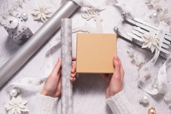 Kobiece ręce trzymać pudełko na prezenty w srebrze i bieli na Boże Narodzenie. Makieta — Zdjęcie stockowe