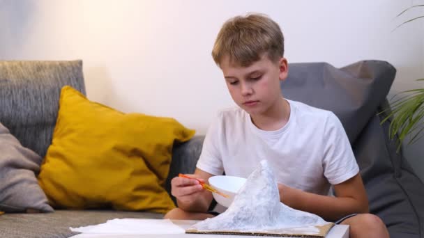 Schoolboy makes creative project in form of papier mache mountain. — Stock Video