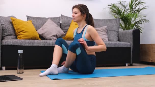 Hermosa mujer joven haciendo ejercicios de fitness mientras mira un ordenador portátil — Vídeos de Stock