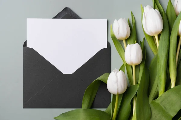 Carte blanche vierge dans une enveloppe et bouquet de tulipes blanches. Moquette papier blanc invitation ou carte de vœux. — Photo