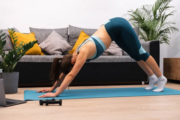Тонка молода жінка робить вправи на гімнастичному килимку вдома — стокове фото